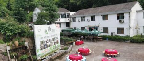 A courtyard with round tables and chairs, surrounded by a white building with a green roof.
