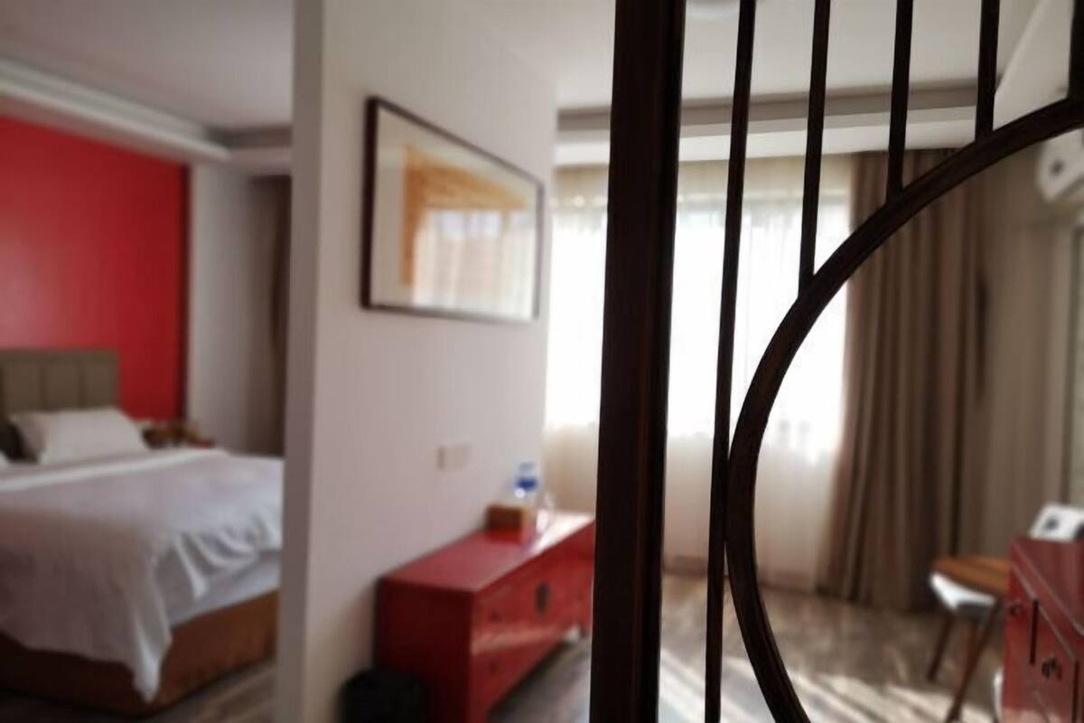 Une chambre d’hôtel avec un lit, une commode rouge et une fenêtre avec des rideaux.
