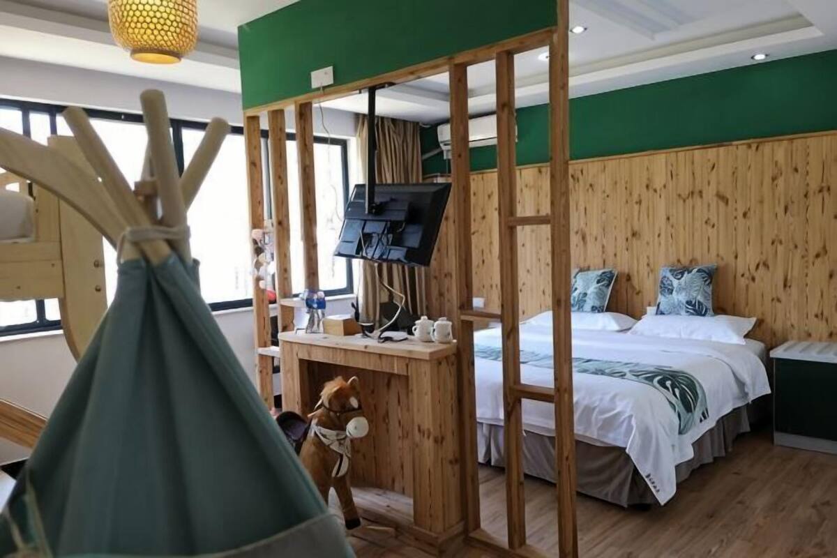 Une pièce comprenant un lit, un bureau avec une télévision, une cloison en bois et une fenêtre.
