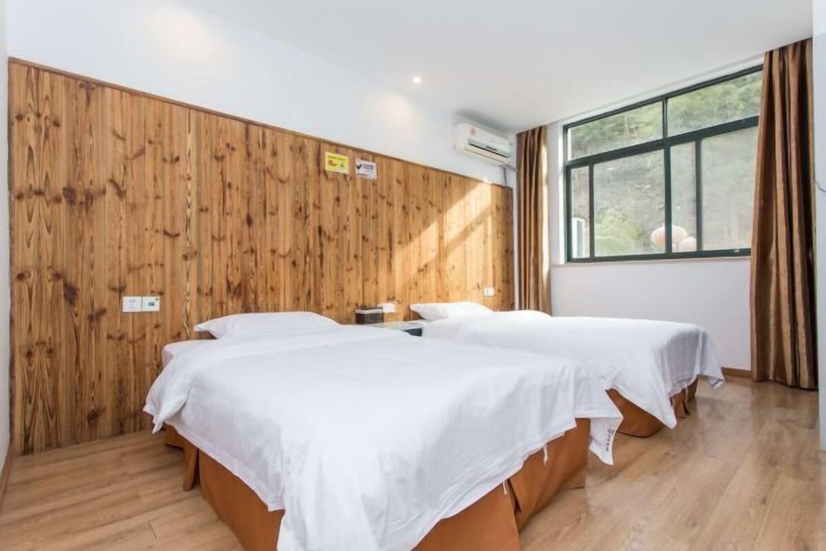 Une chambre avec deux lits, des murs en bois, une fenêtre avec des rideaux et un appareil de climatisation.