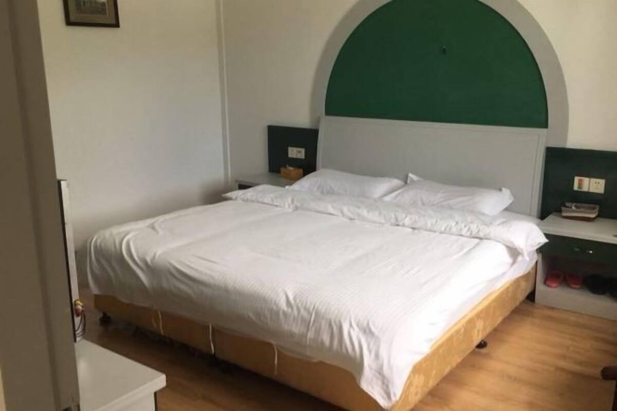 Une chambre avec un lit simple, surmontée d’une arche verte au-dessus de la tête de lit, avec une literie blanche et des tables de chevet équipées de lampes.