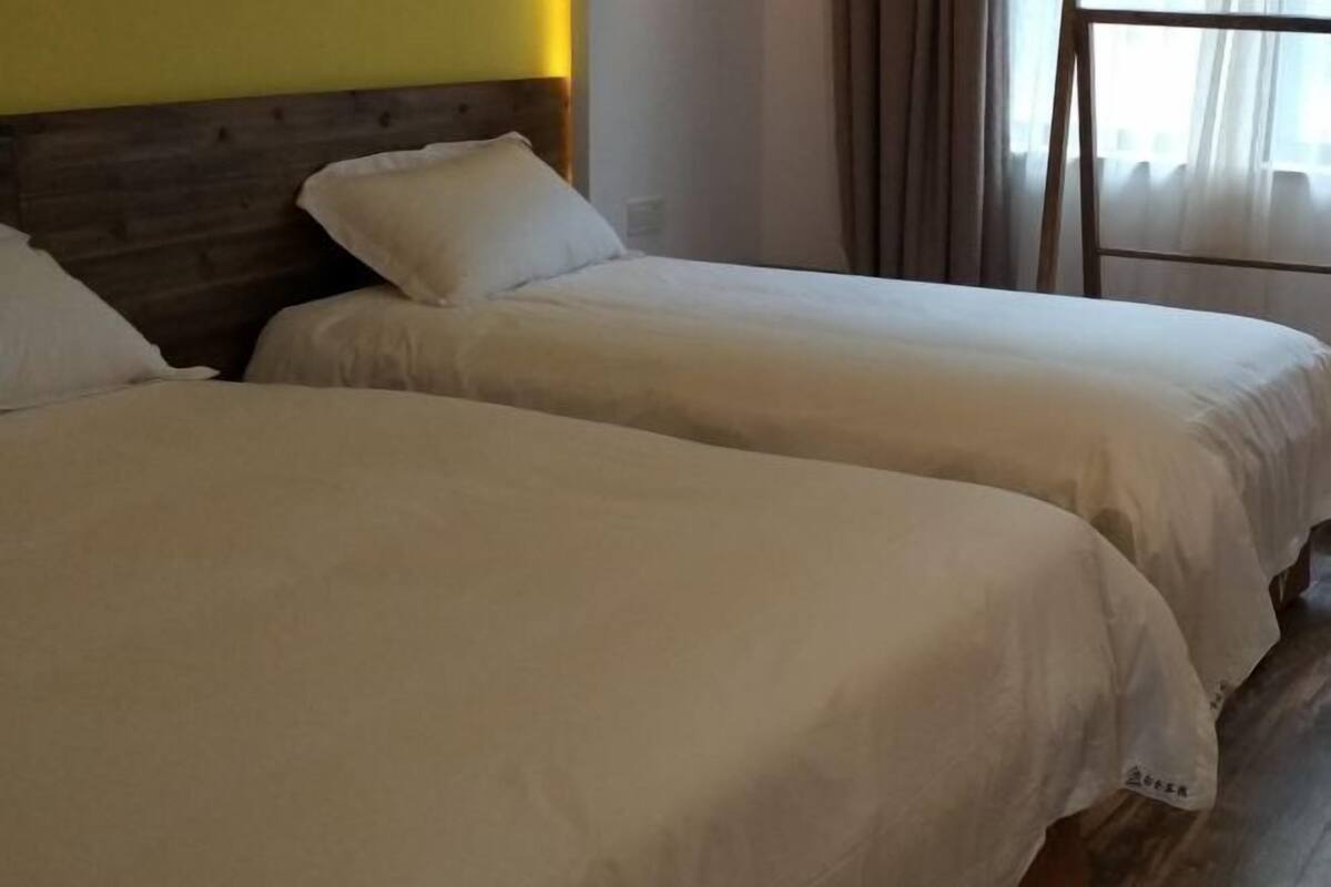 Deux lits simples avec des têtes de lit en bois, du linge de lit blanc et une fenêtre avec des rideaux.