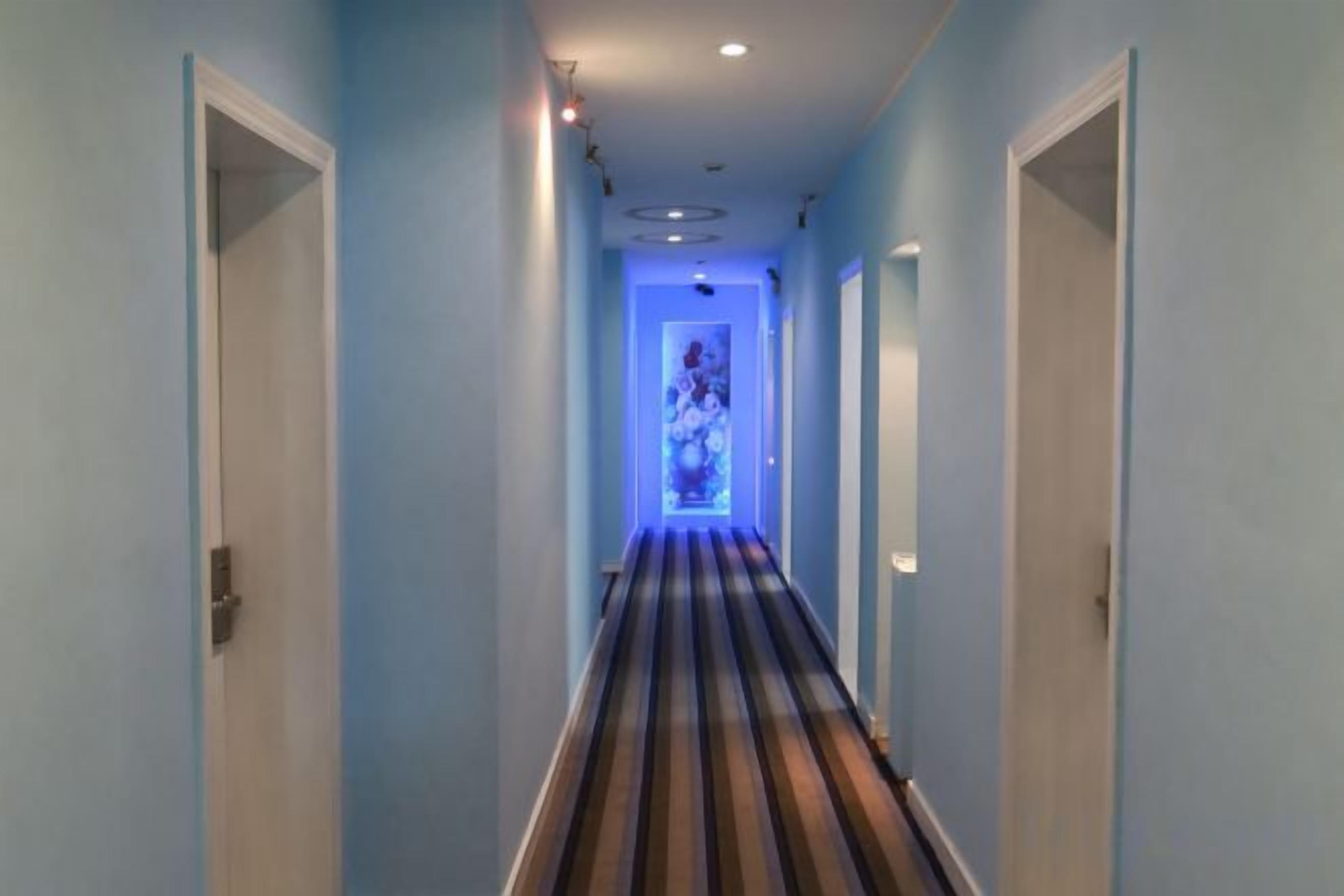 Un pasillo estrecho con alfombra a rayas, puertas a ambos lados y una fuente de luz al final.