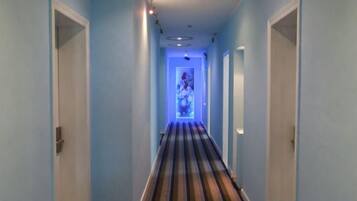Un pasillo estrecho con alfombra a rayas, puertas a ambos lados y una fuente de luz al final.