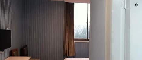 A hotel room with a bed, a desk, a chair, a television, and a window with curtains.