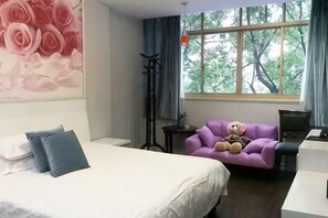 A hotel room with a bed, a purple sofa with a teddy bear, a window with a view of trees, and a coat rack. - Jiangbin Hotel (Shaoxing)