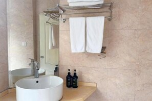 A bathroom with a large white sink, a mirror, a towel rack with folded towels, and two bottles on the counter. - Jiangbin Hotel (Shaoxing)