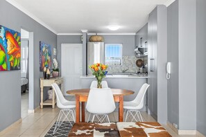 Une cuisine moderne avec des meubles blancs, un coin repas avec une table en bois et des chaises blanches, et un vase de fleurs sur la table.