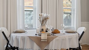 A dining table set with plates, glasses, a vase with dried flowers, and a loaf of bread. - The Tellico Plains Inn, Historic Boutique Hotel, The Babcock Room (Tellico Plains)