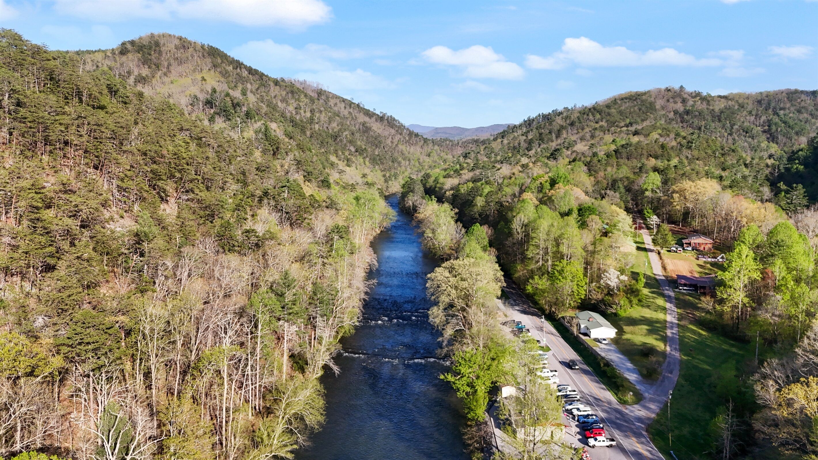 A river running through a forested valley with a road and parking area on one side.