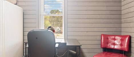 A small room with a desk, a red chair, and a window with blinds.