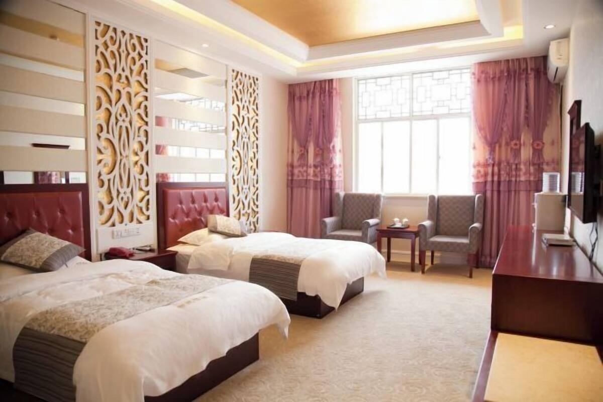 A hotel room with two beds, a desk, a chair, and a TV.