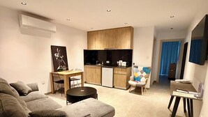 Una sala de estar moderna con un sofá modular, una zona de comedor con una mesa pequeña y una kitchenette.