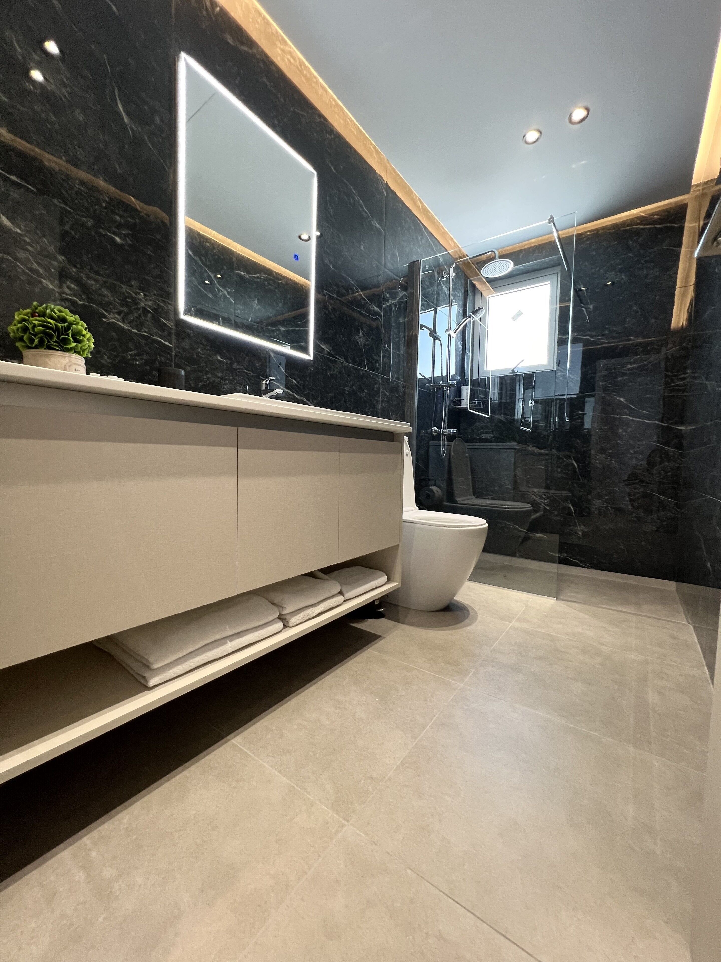 A modern bathroom with a marble wall, a large mirror, a glass shower enclosure, and a white toilet.