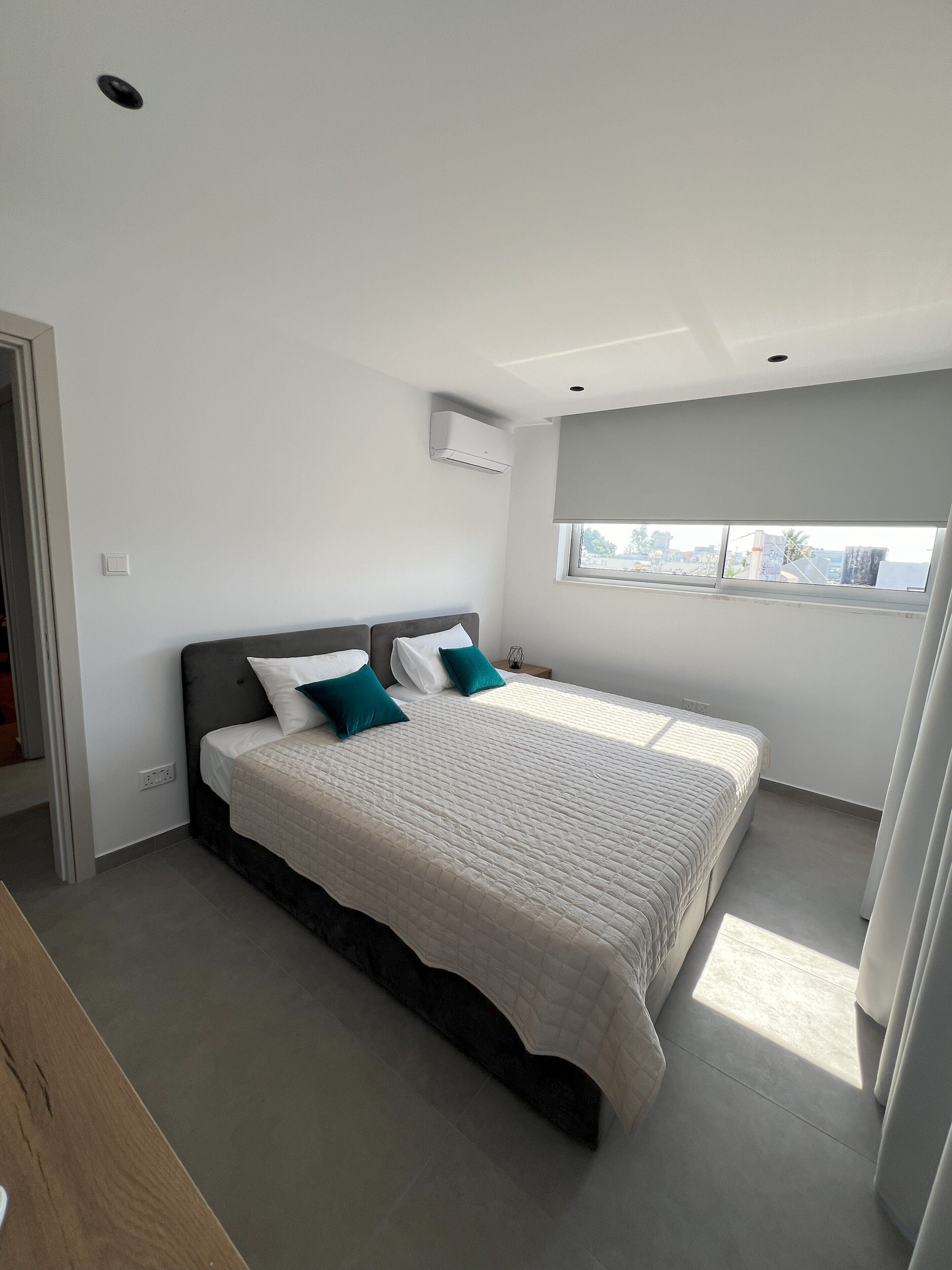 A bedroom with a large bed, a window, and an air conditioning unit.