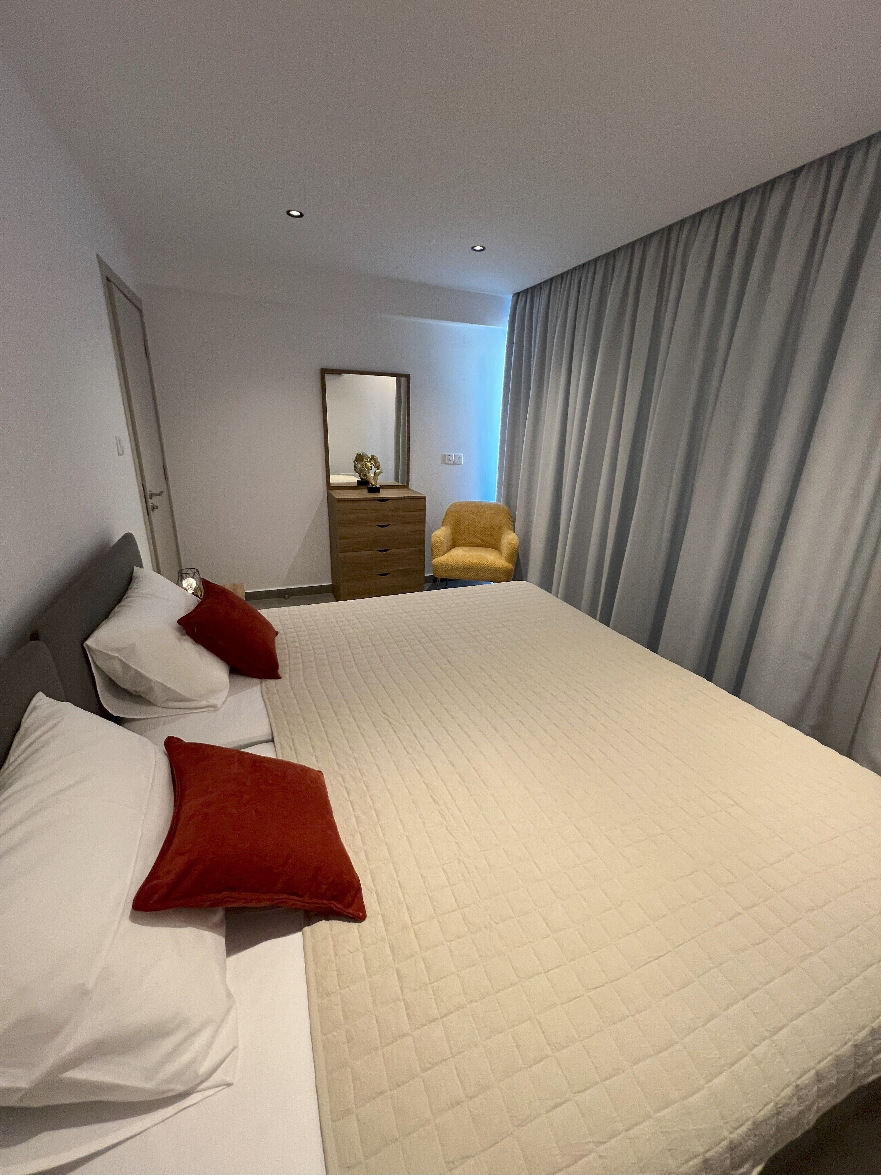 A hotel room with a large bed, two pillows, a dresser, a chair, and a mirror.