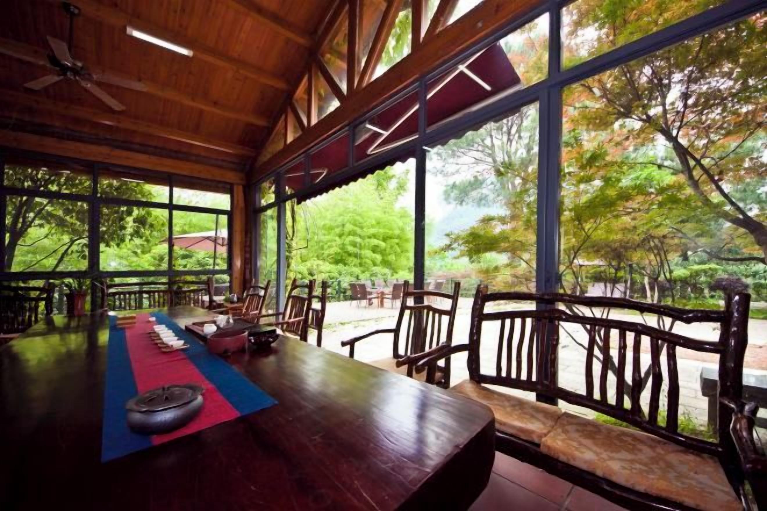 Un comedor interior con una larga mesa, sillas y vistas a árboles a través de amplios ventanales.