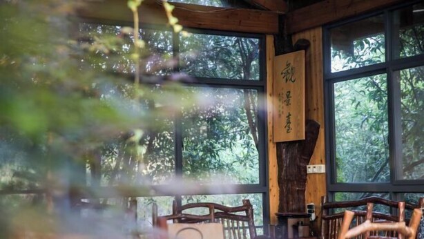 A wooden interior with large windows, a table with chairs, and a sign with Chinese characters. - Wuyishan Guanjing Shanfang Hotel (Wuyishan)