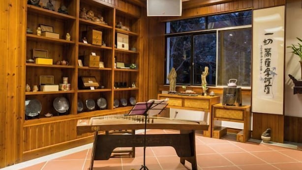 A traditional Japanese room with wooden shelves displaying various items, a tatami mat floor, and a large window with a view of trees. - Wuyishan Guanjing Shanfang Hotel (Wuyishan)