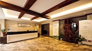 A reception area with a marble floor, wooden ceiling beams, a reception desk, and a statue. - Wuyishan Guanjing Shanfang Hotel (Wuyishan)