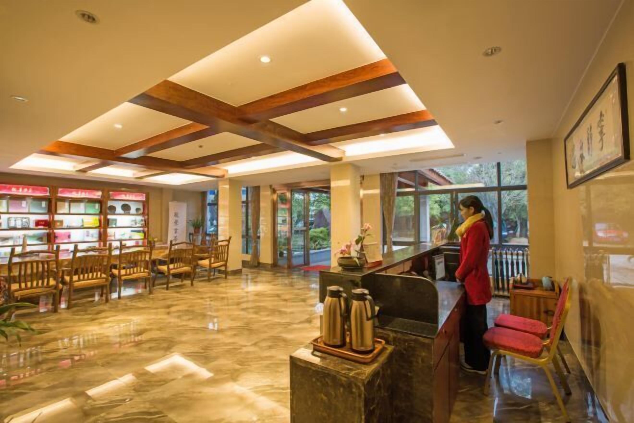 A hotel lobby with a marble floor, wooden ceiling beams, a reception desk, and a bookshelf with various items.