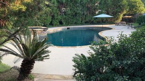 Une piscine entourée d’une végétation luxuriante, avec un sentier en pierre qui y mène.