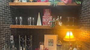 Un espace bar avec des étagères remplies de bouteilles et de verres, et une pancarte sur laquelle on peut lire : « ÊTRE gentil, c’est bien, mais être un peu coquin, c’est encore mieux. »