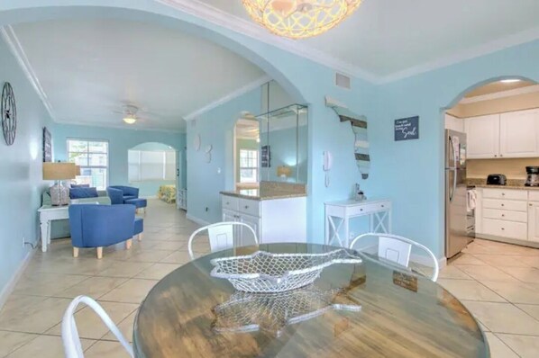 A spacious living area with a round dining table, blue sofas, and a kitchen area with white cabinets.