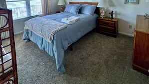 A bedroom with a bed, two nightstands, a dresser, a chair, and a window with curtains.