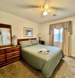 Une chambre à coucher comprenant un lit, une commode, un miroir, une lampe et un ventilateur de plafond.