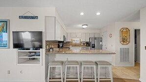 A modern kitchen with a large island, white cabinetry, and a flat-screen TV.