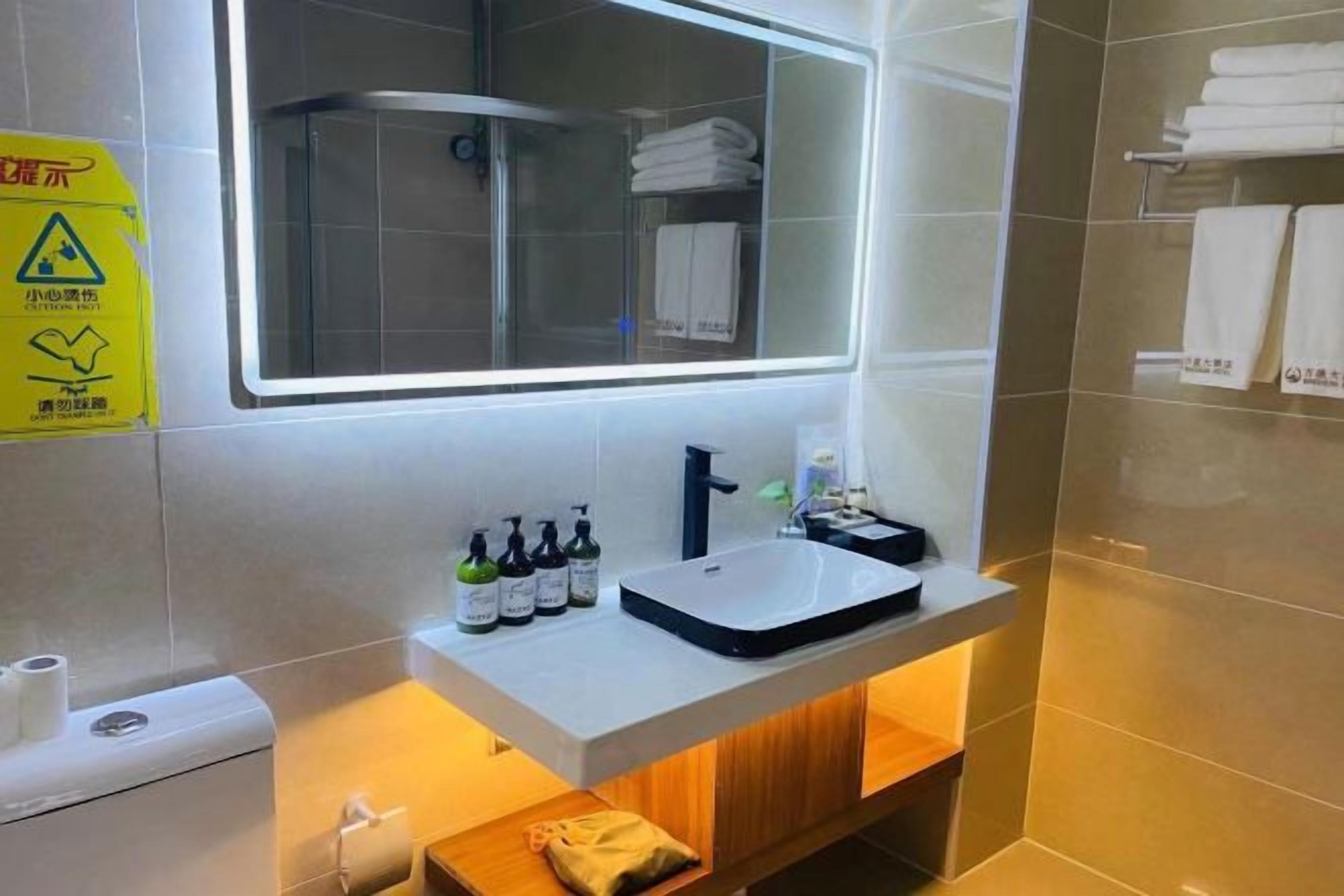A bathroom with a white sink, a mirror, and a shower. There are toiletries on the sink and towels on the wall.