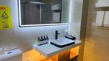 A bathroom with a white sink, a mirror, and a shower. There are toiletries on the sink and towels on the wall.