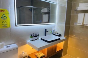 Un baño con un lavabo blanco, un espejo y una ducha. Hay artículos de aseo en el lavabo y toallas en la pared.