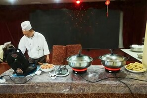A chef preparing food at a counter with a food processor, bowls, and a large pot. - Wansheng Hotel (Yuanqu)