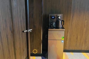 A compact kitchenette with a coffee maker, a small refrigerator, and a door with a handle. - Wansheng Hotel (Yuanqu)