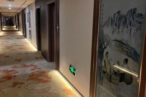 Pasillo de hotel con alfombra estampada, puertas y una obra de arte colgada en la pared.