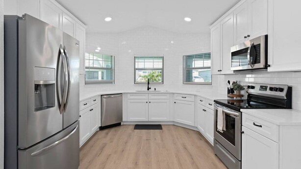 A modern kitchen with white cabinets, stainless steel appliances, and a wooden floor. -  - HIDDEN GEM - Spacious, minimal and clean! Legoland + Disney (Wahneta)