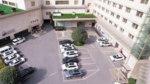 A parking lot with multiple rows of cars, a central tree, and a building with multiple floors and windows. - Bell Tower Hotel (Xi'an)
