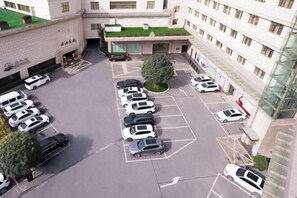 A parking lot with multiple rows of cars, a central tree, and a building with multiple floors and windows. - Bell Tower Hotel (Xi'an)