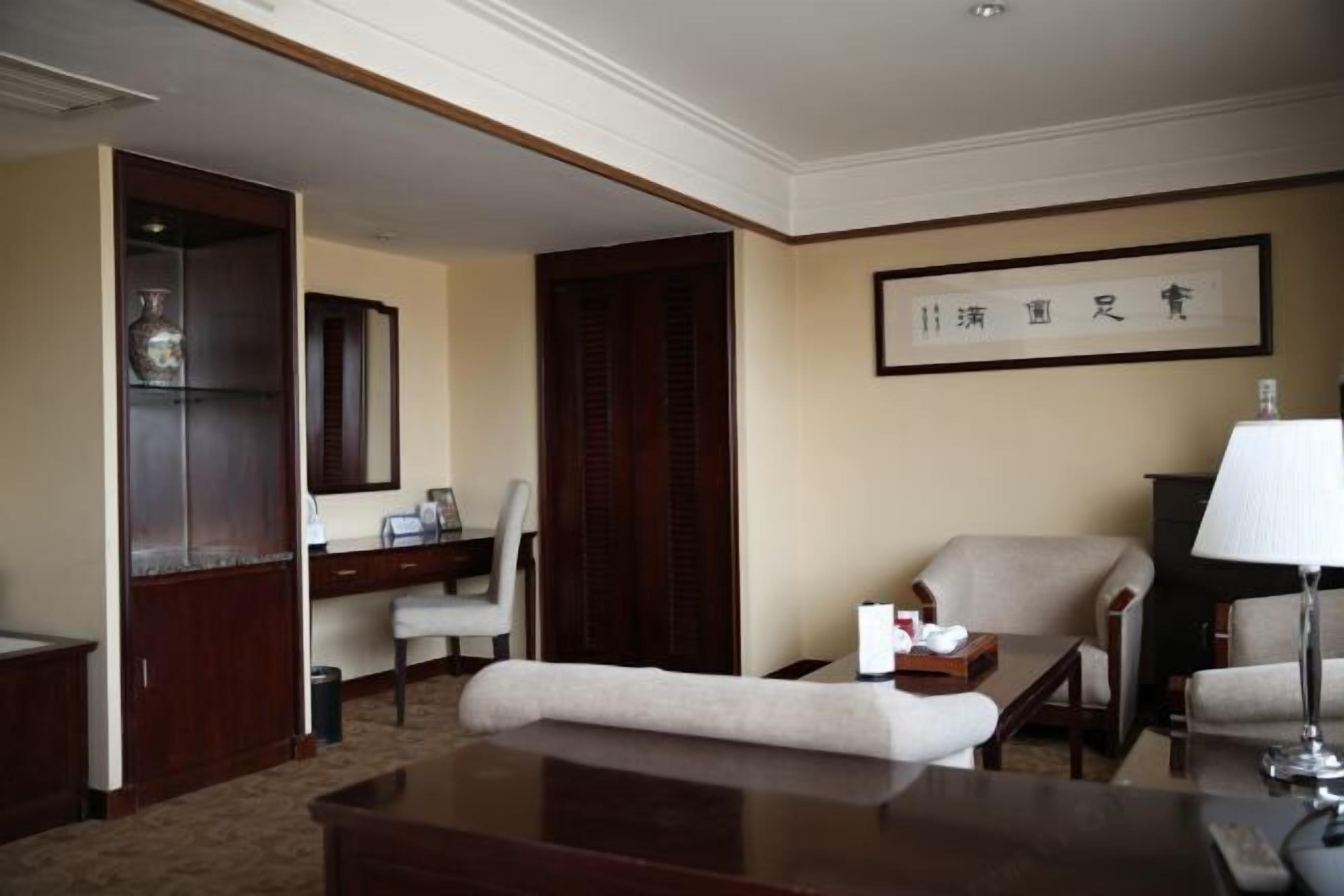 A hotel room with a desk, two chairs, a sofa, a lamp, and a framed artwork on the wall.