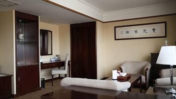 A hotel room with a desk, two chairs, a sofa, a lamp, and a framed artwork on the wall.