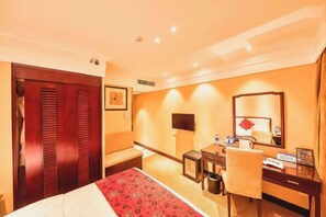 Una habitación de hotel con cama, escritorio, silla, televisor y espejo.