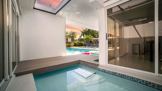 Una piscina interior moderna con vistas a un atardecer y palmeras.