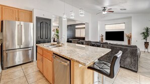 Eine moderne Küche mit Edelstahlkühlschrank, Holzschränken, Granit Arbeitsplatten und einer integrierten Kochinsel mit Barhocker.