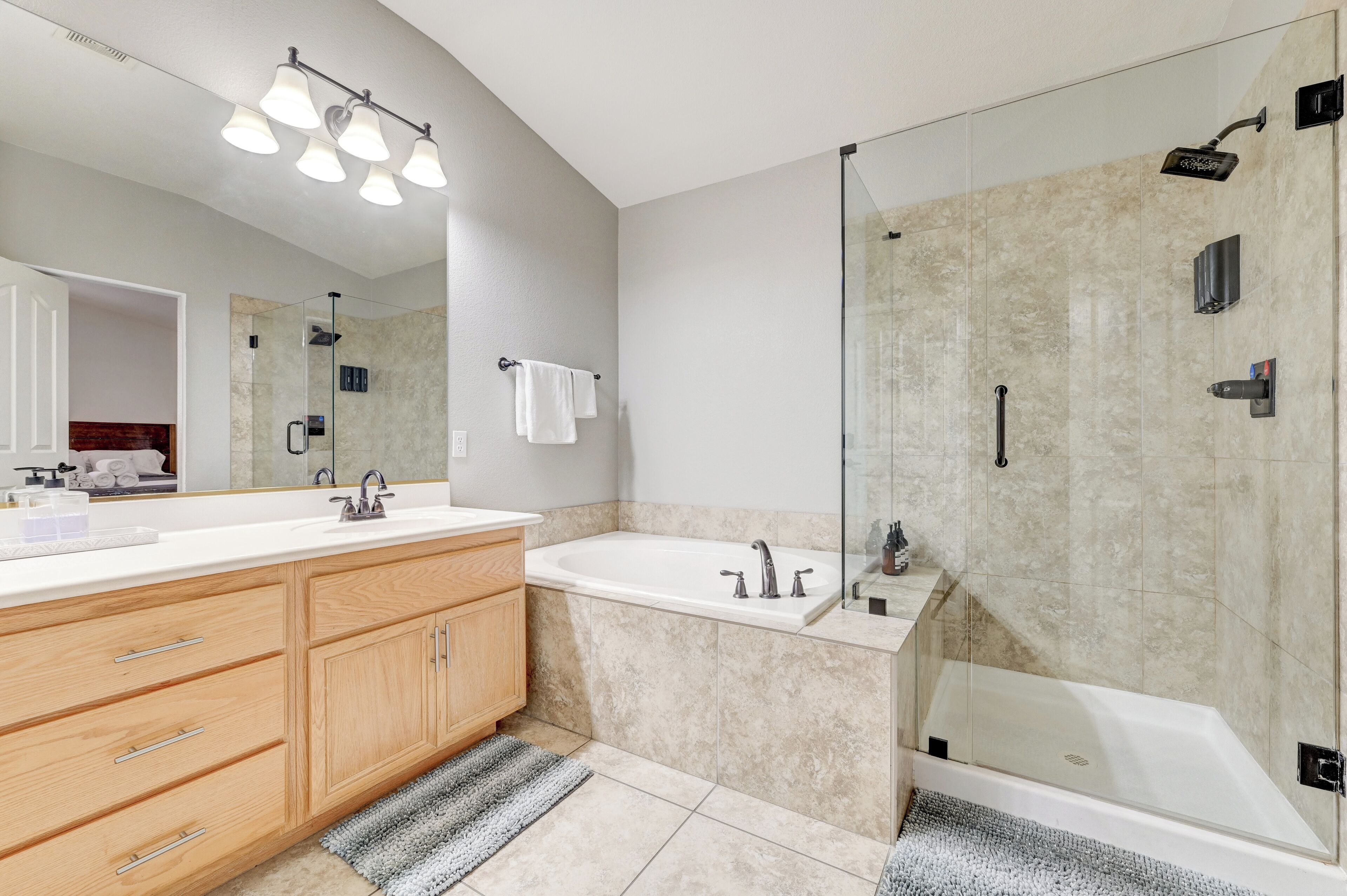 A modern bathroom with a large mirror, a vanity with drawers, a bathtub, and a glass-enclosed shower area.