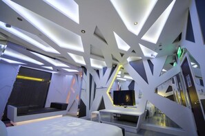 Moderni hotellihuone, jossa on ainutlaatuinen, geometrisesti muotoiltu kattorakenne, litteänäyttöinen televisio ja kuviollinen päätyosaan varustettu sänky.