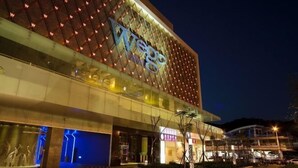 Un edificio moderno con un'insegna 'Vega' ben visibile, caratterizzato da una facciata geometrica e finestre illuminate.