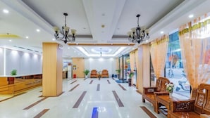 Um hall amplo com área de estar central, balcão de recepção e uma grande janela com cortinas.