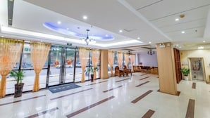 Um saguão de hotel com balcão de recepção, área de estar e janelas amplas com cortinas.
